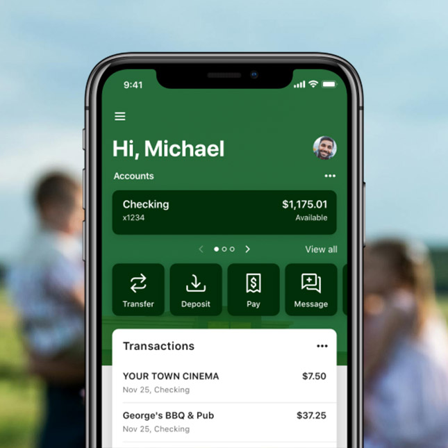 A phone showing the mobile banking app with family blurred in the background.