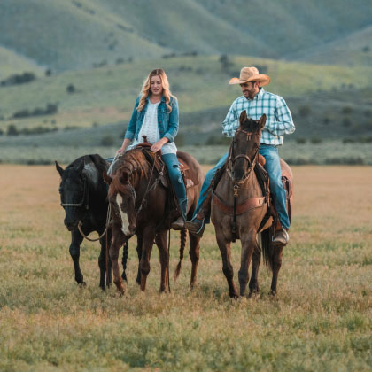 man and woman riding horses in a field