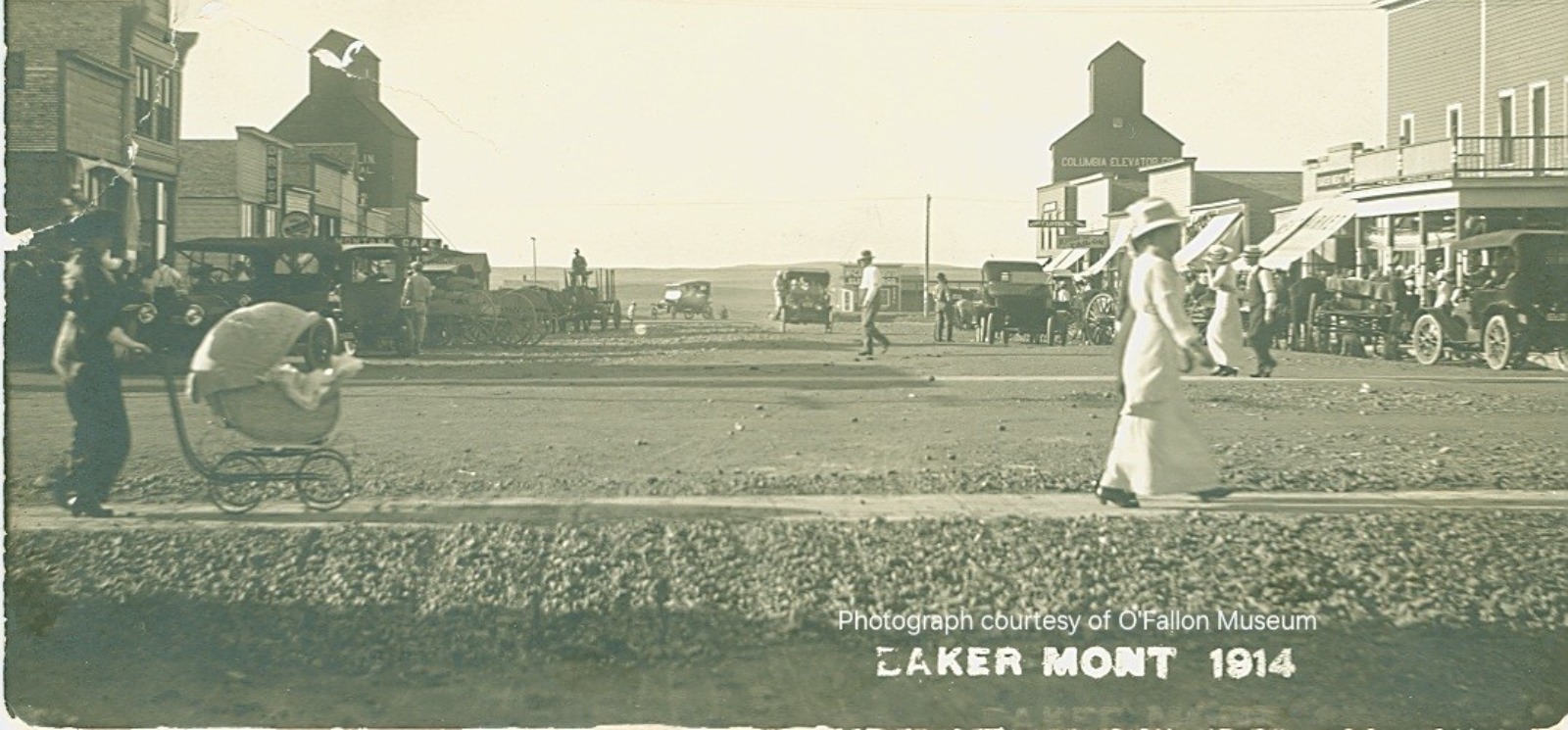 Mother pushing baby in a stroller in downtown Baker, MT 1914.